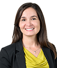 Headshot: Dark haired woman in black Jacket and yellow top smiling at the camera.