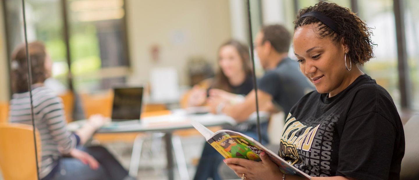 Fast Track Program Banner female student wearing a black Oakland University shirt, reading a book