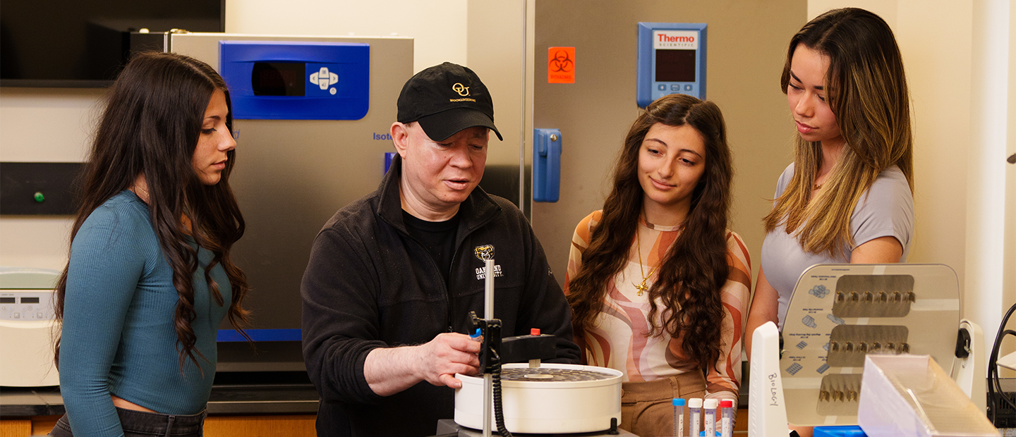 Summer Undergraduate Research Program Three women observing an instructor working in a lab.