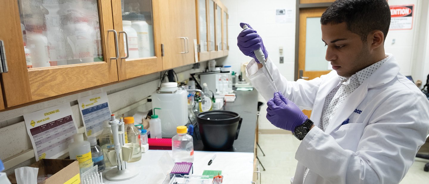 BIO-22752_Premed_prehealthStudies.jpg A man wearing a white lab coat, holding a medical syringe in a medical lab.