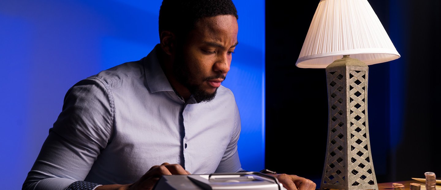 A man seated at a desk with a lamp, using a large calculator. A man seated at a desk with a lamp, using a large calculator.