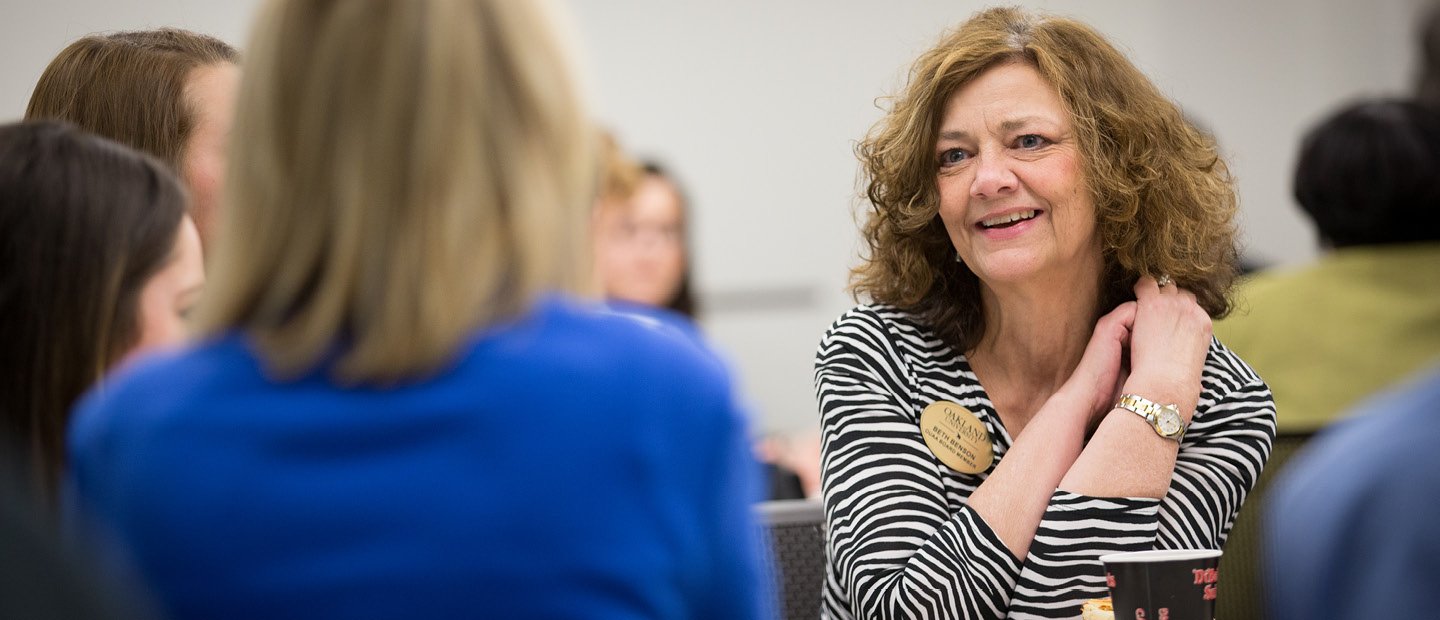 A woman wearing a name tag, seated, talking to three other women A woman wearing a name tag, seated, talking to three other women.