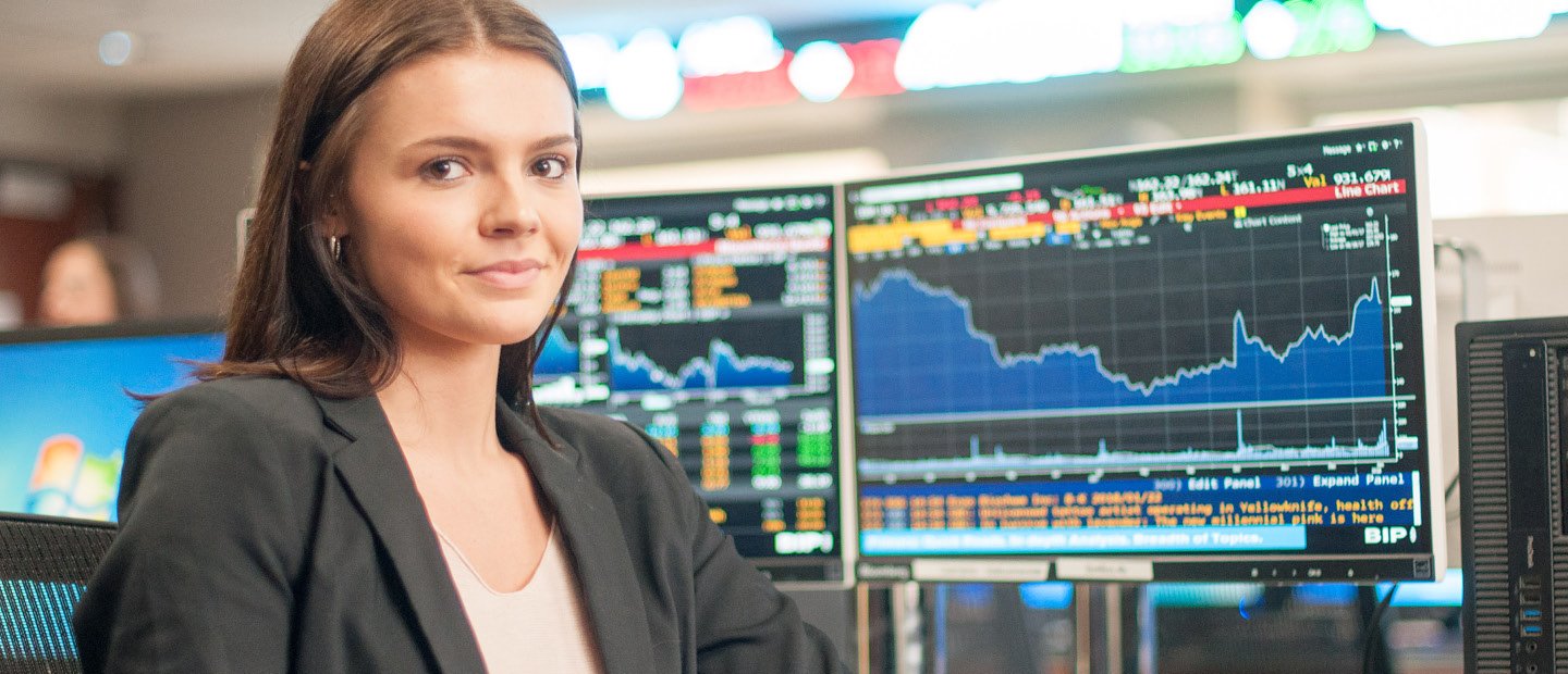 A woman seated in front of computer screens with colorful charts of data. A young woman seated in front of computer screens with colorful charts of data displayed.