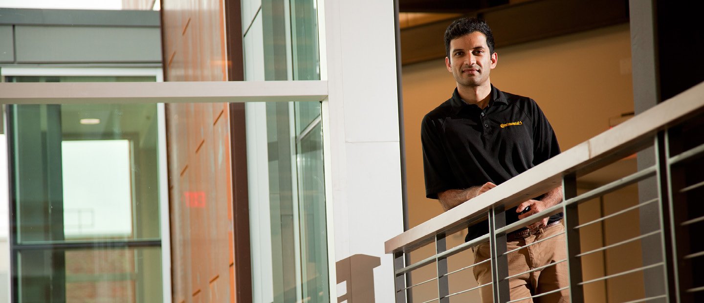 SBA-22398_BusEssentials.jpg A man leaning on a railing in a hallway, looking down at the camera.