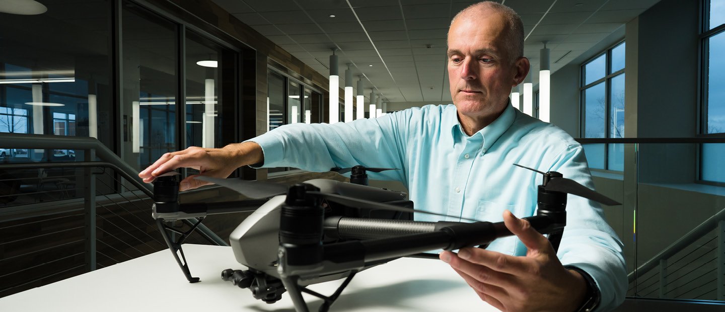 A man seated at a table, holding a drone A man seated at a table, holding a drone.