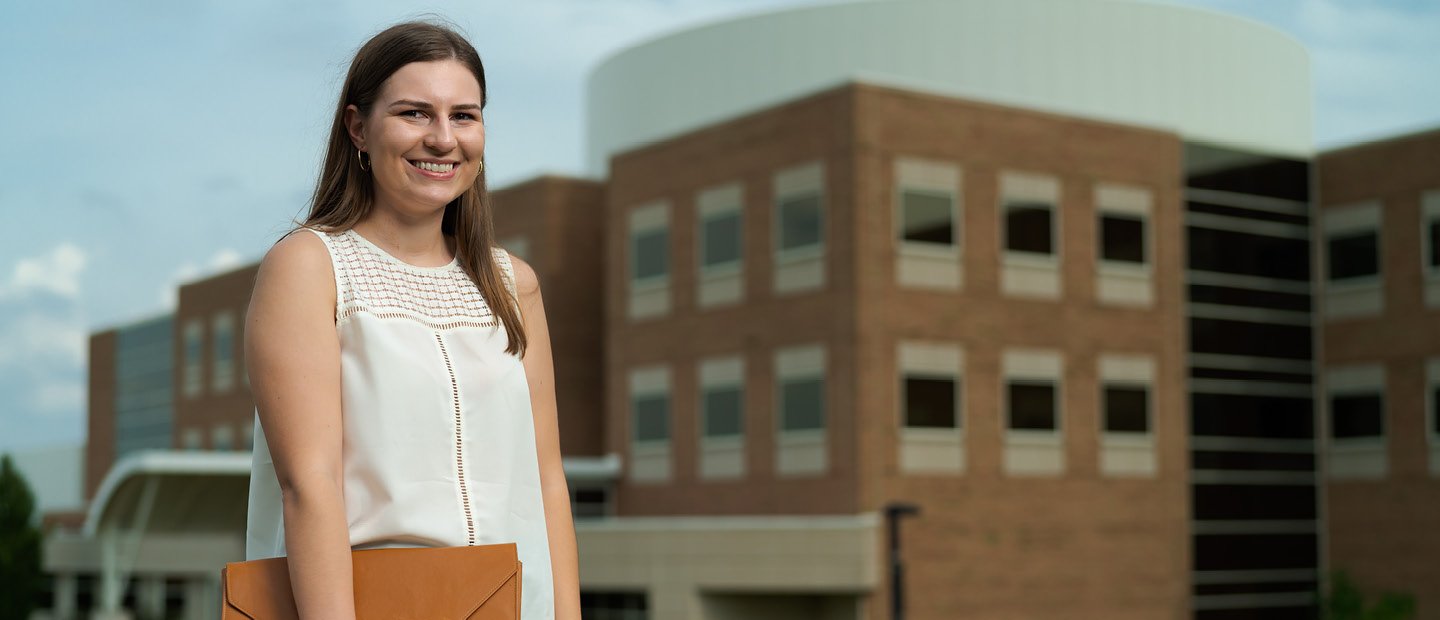 A woman holding standing in front of a building at Oakland University. A woman holding a brown folder standing in front of a brown building at Oakland University.