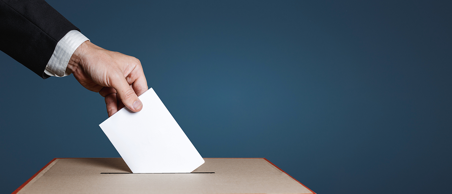Voting in Michigan banner Closeup of hand putting ballot in a ballot box
