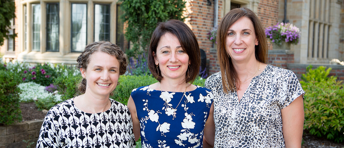Contact Us Banner Three women, smiling, standing together in front of garden