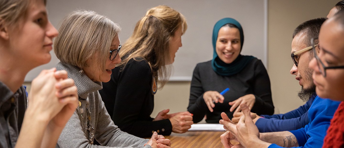 Grad Student Series banner A group of adults seated at a rectangular table, having a conversation.