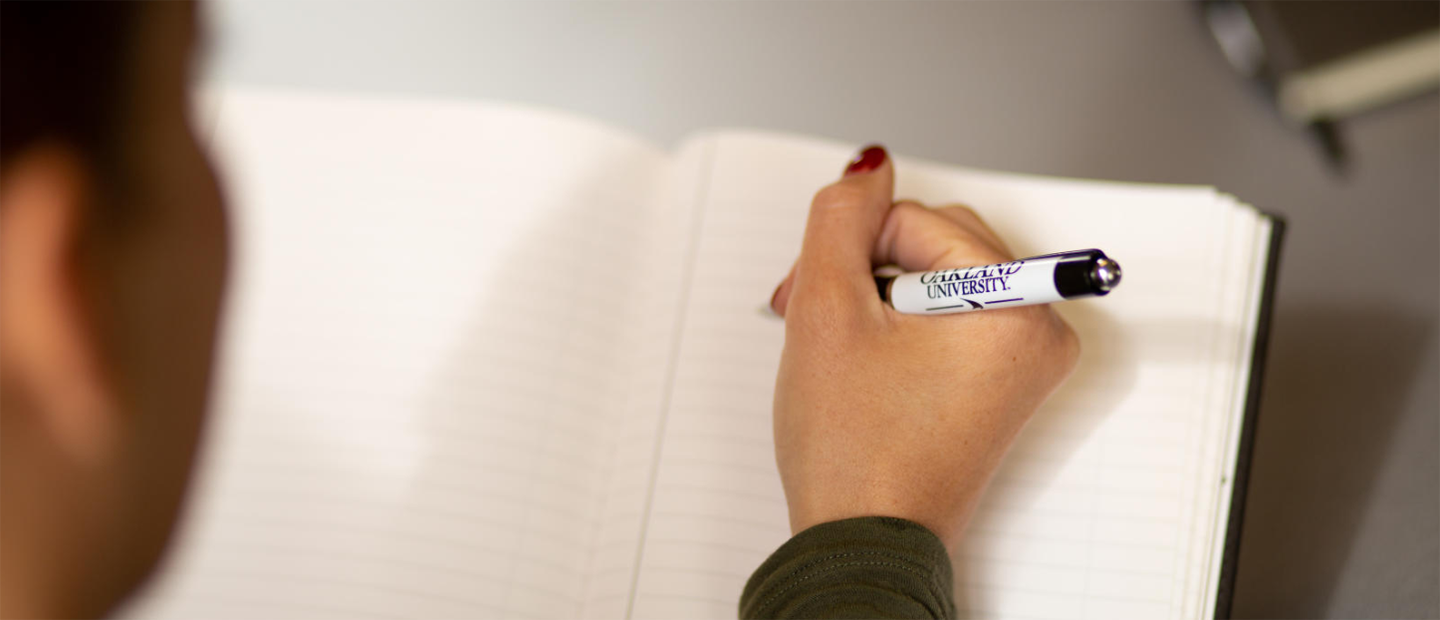 Syllabus Guides Banner A person's hand holding an Oakland University pen over an empty notebook.