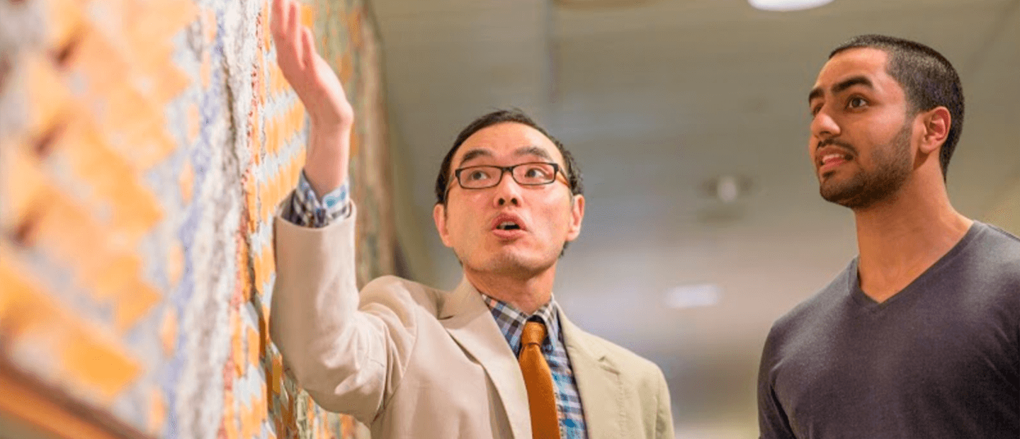 Teaching Resources Banner A professor gesturing to a colorful wall as a young man looks at it.