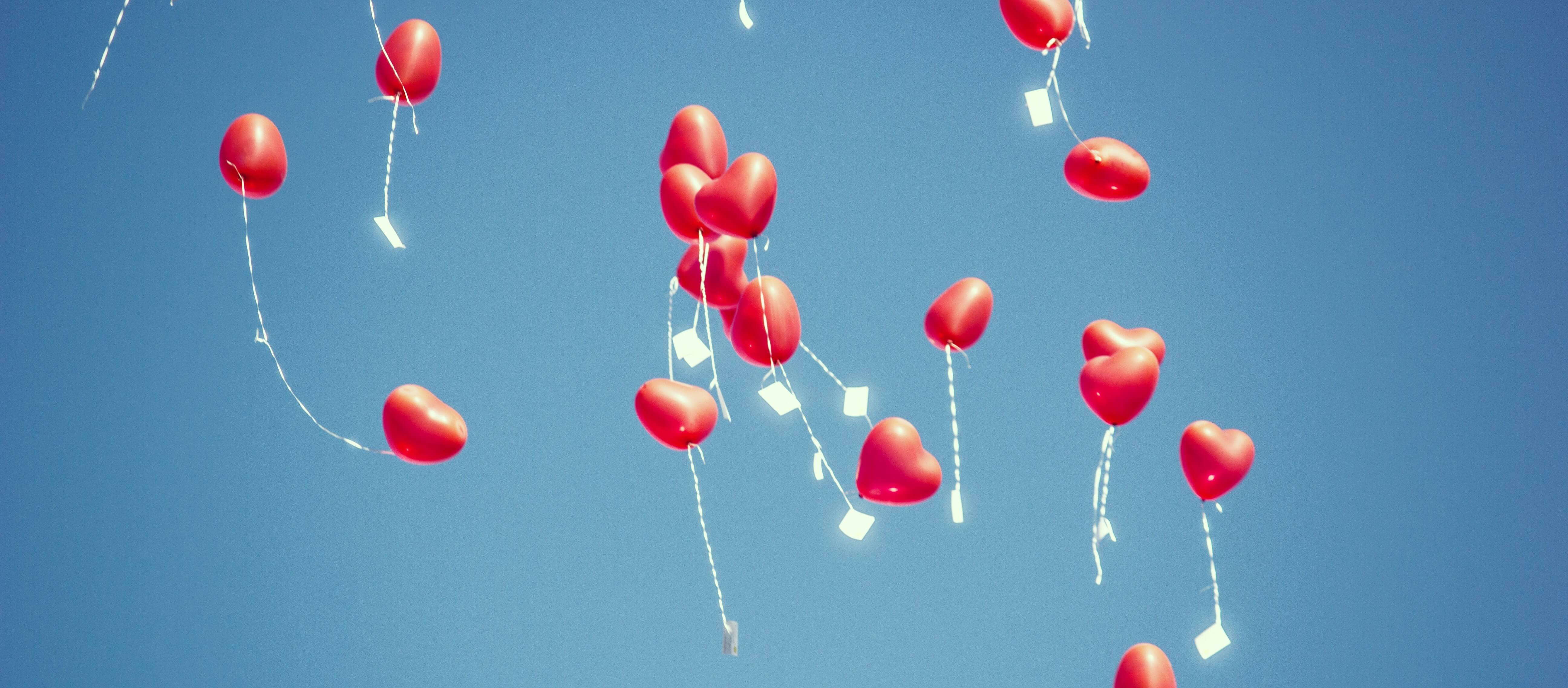 Heart balloons with paper messages attached, floating through the sky