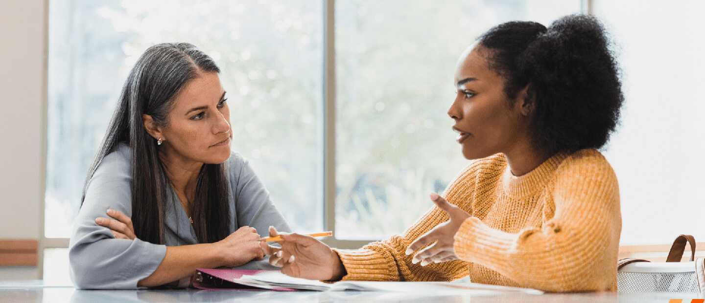 two women sitting at the desk having a conversation