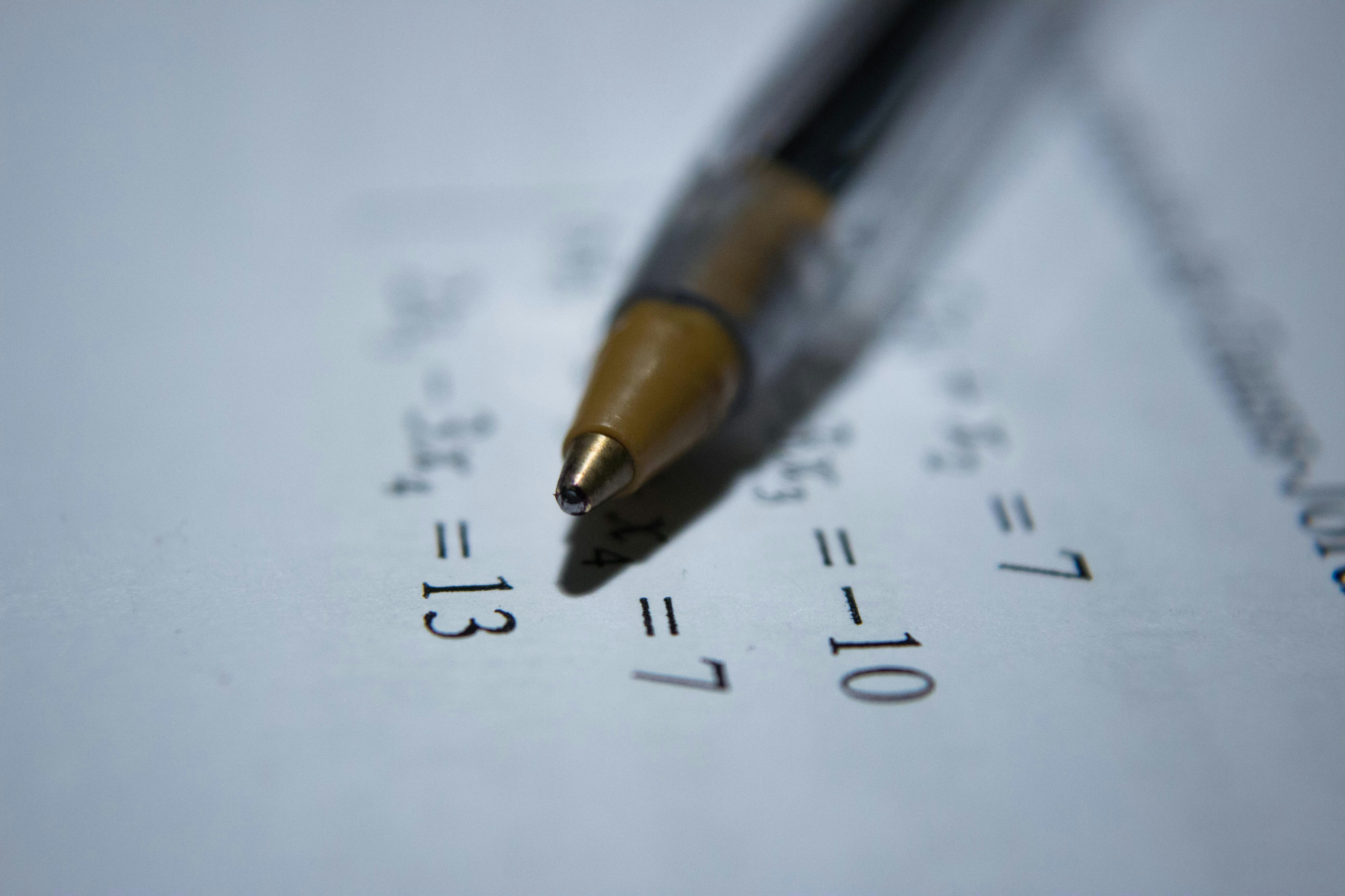 Close-up of a pen resting on a piece of paper with mathematical equations printe