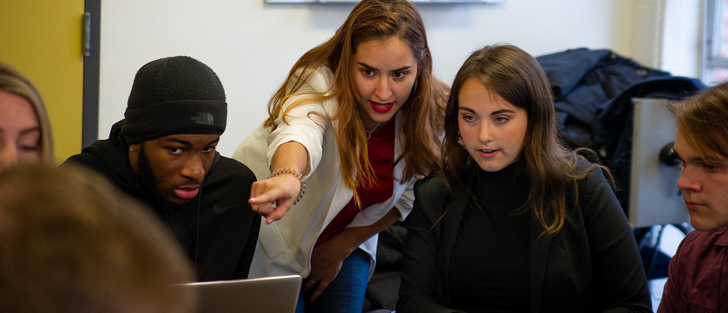 PR and Strategic Communication, B.A. Banner A group of people looking at something on a laptop that one woman is pointing to.