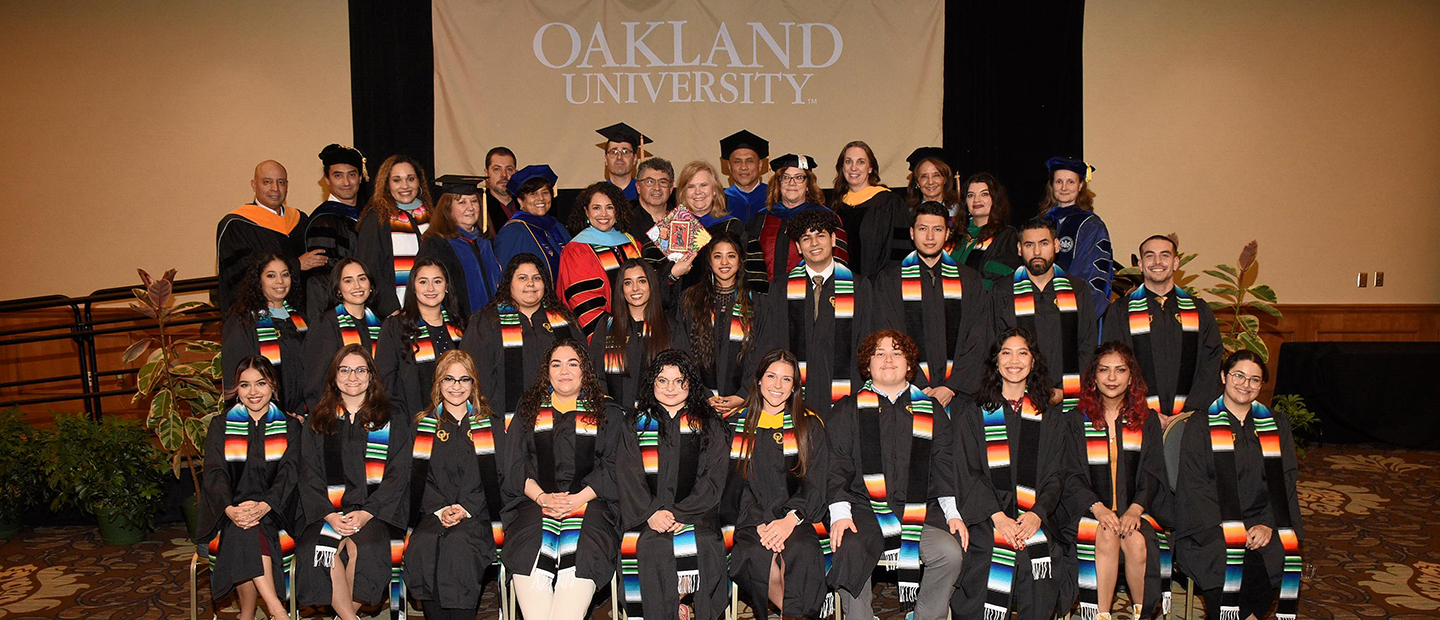 Latina/o/x graduation banner Group of students in graduation gowns at Latina/o/x graduation ceremony
