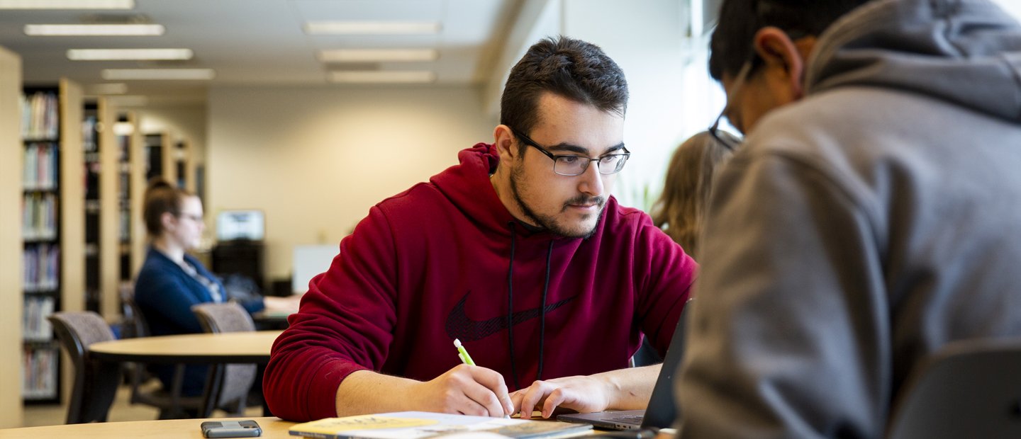 Student taking notes A male student looking at his laptop is writing notes on a pad of paper