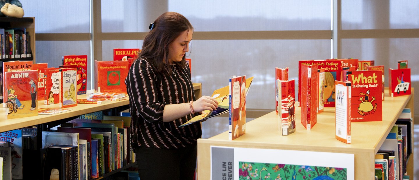 woman reviews book A woman standing by a bookshelf reviews a children picture book.