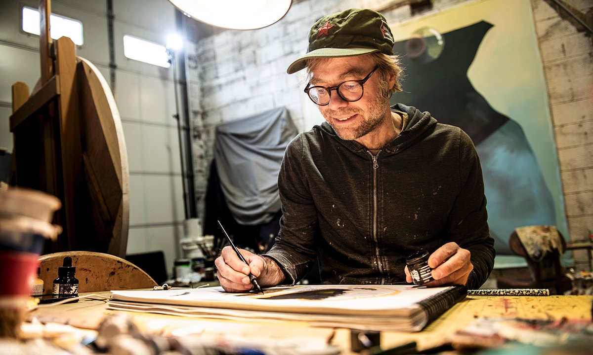 A man sits at a table painting.
