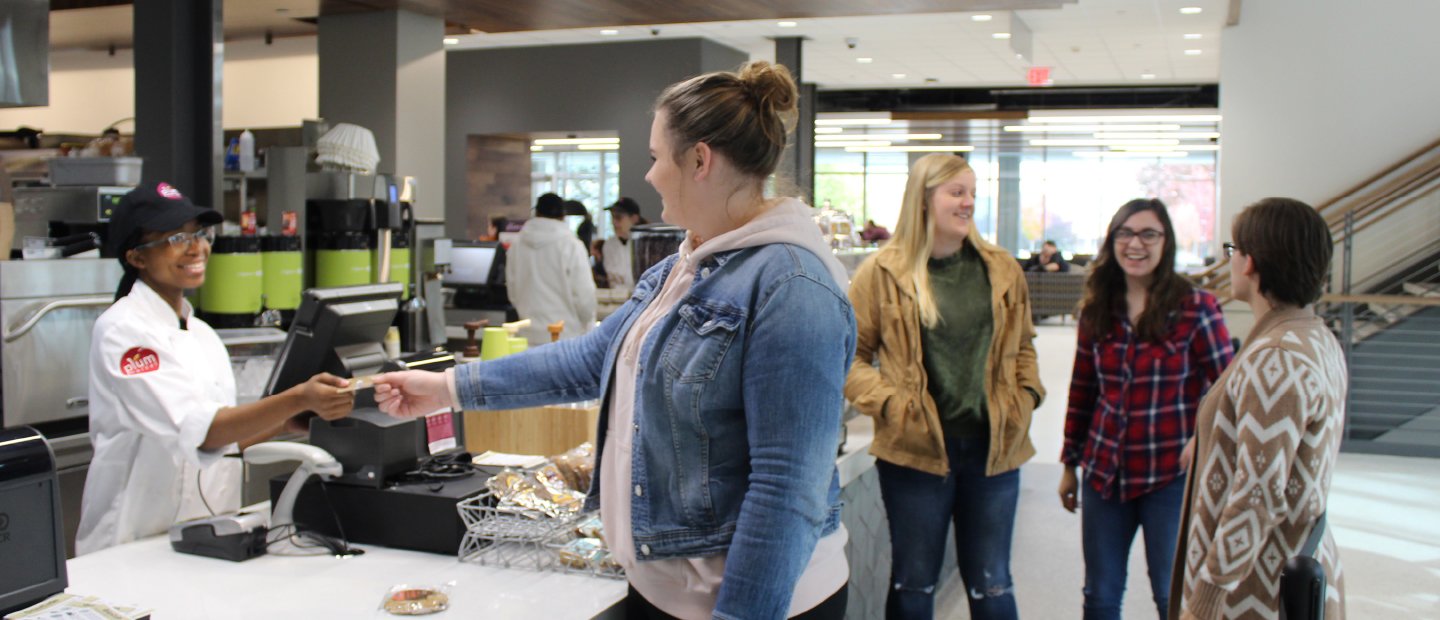 GrizzCa$h Banner woman handing a card over a counter to a cashier in a dining center