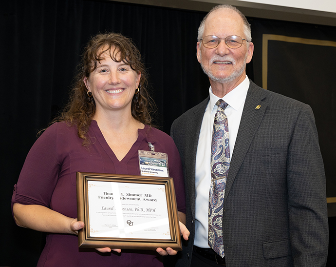 A woman holds framed certificate, pictured with the Dean
