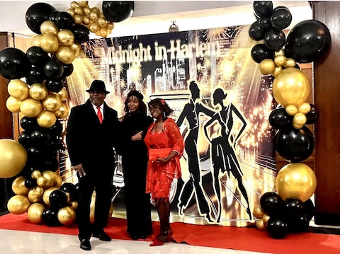 People posing in front of a Midnight in Harlem banner at a formal dancing event