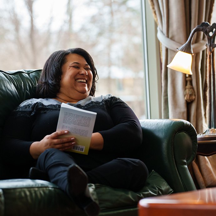 A person in a chair holding a book and laughing