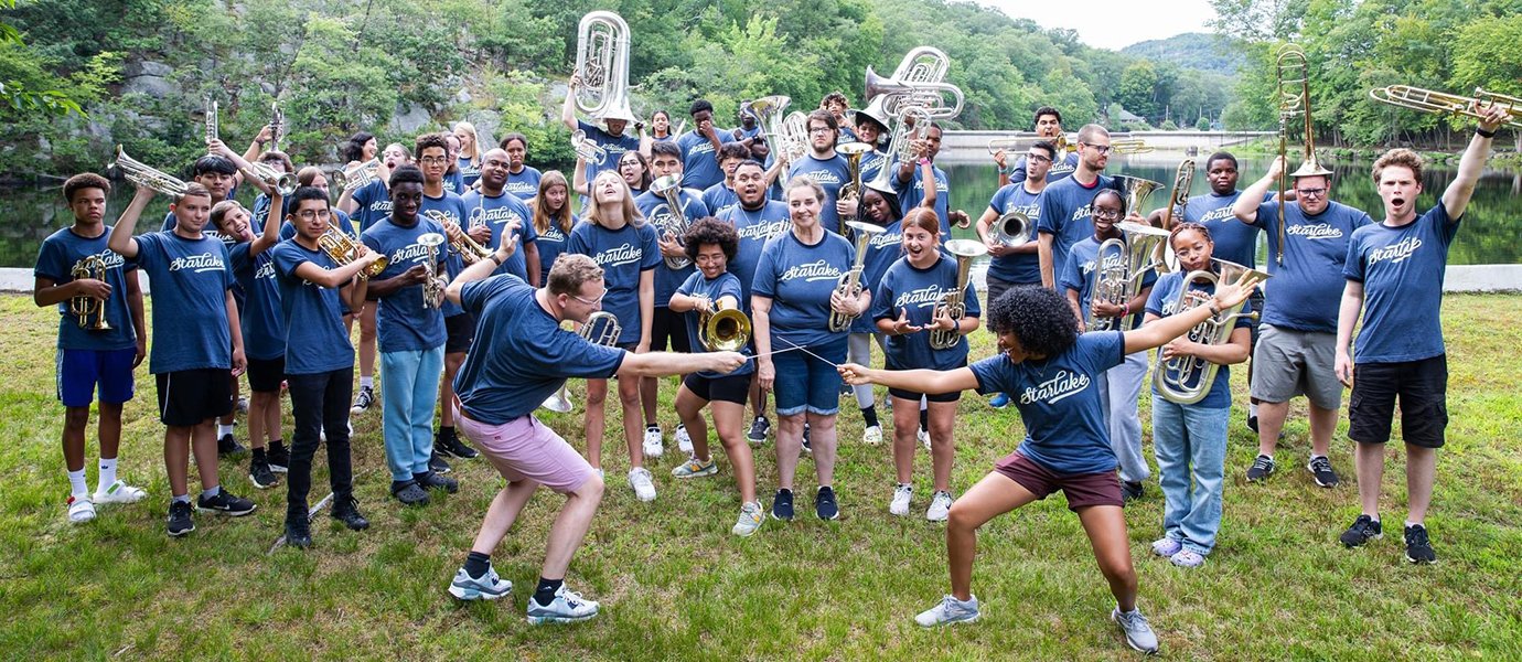 Two people jokingly have a sword fight in front of a crowd of people holding musical instruments