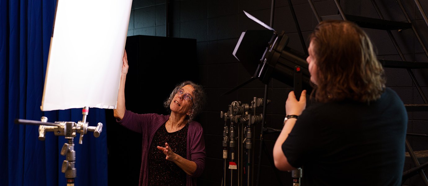 a person talking in front of a person adjusting a light