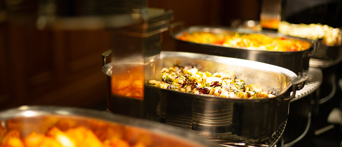 Catering banner A row of silver dishes full of a variety of catered food.