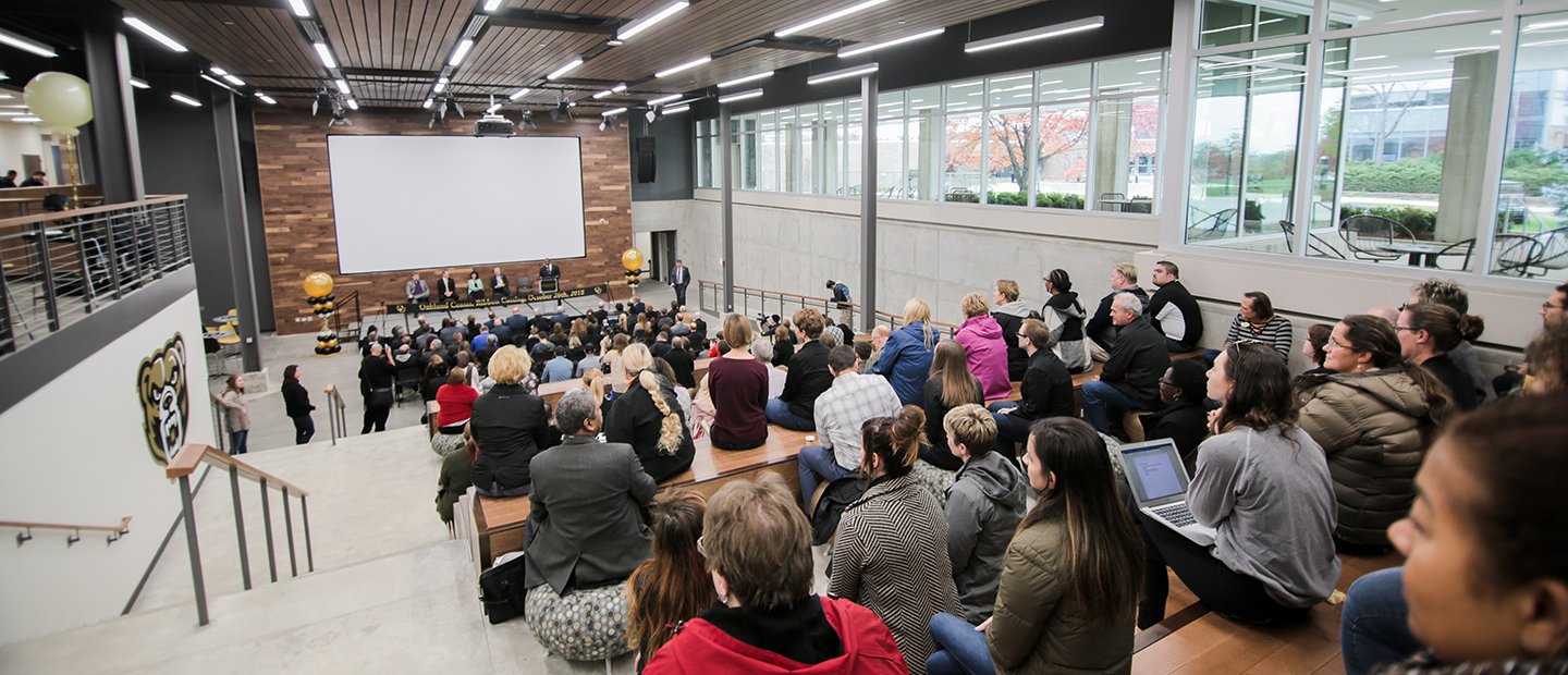 Conferences and Events Banner panel of people seated in front of a large white screen, facing an audience