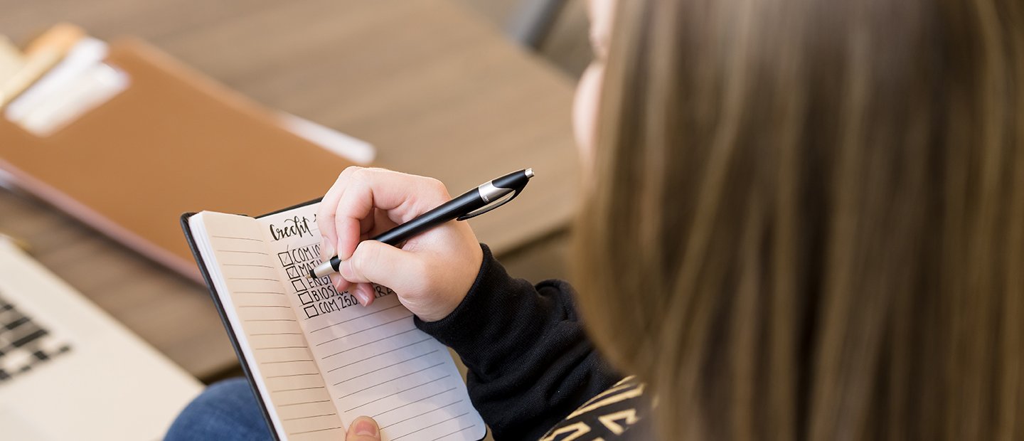 Transfer Information Banner An Oakland University student making check marks next to courses listed in a notebook.