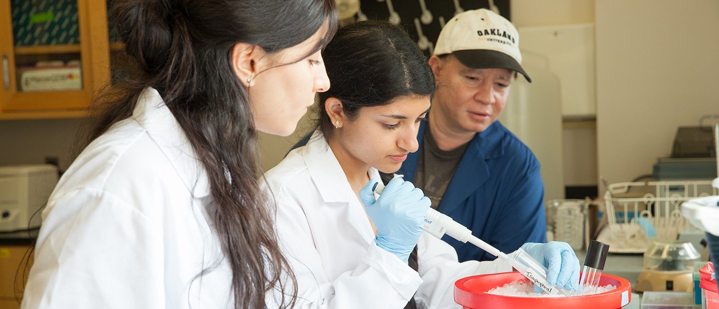 Student Funding Opportunities Banner A woman holding a vial in a lab while two people observe.
