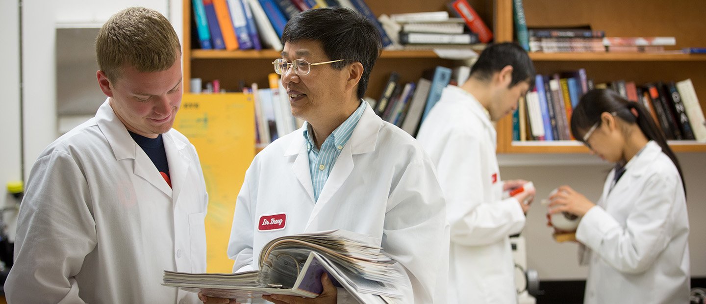 Calendar, Training and Events Banner Four people in white lab coats in front of a shelf of books.