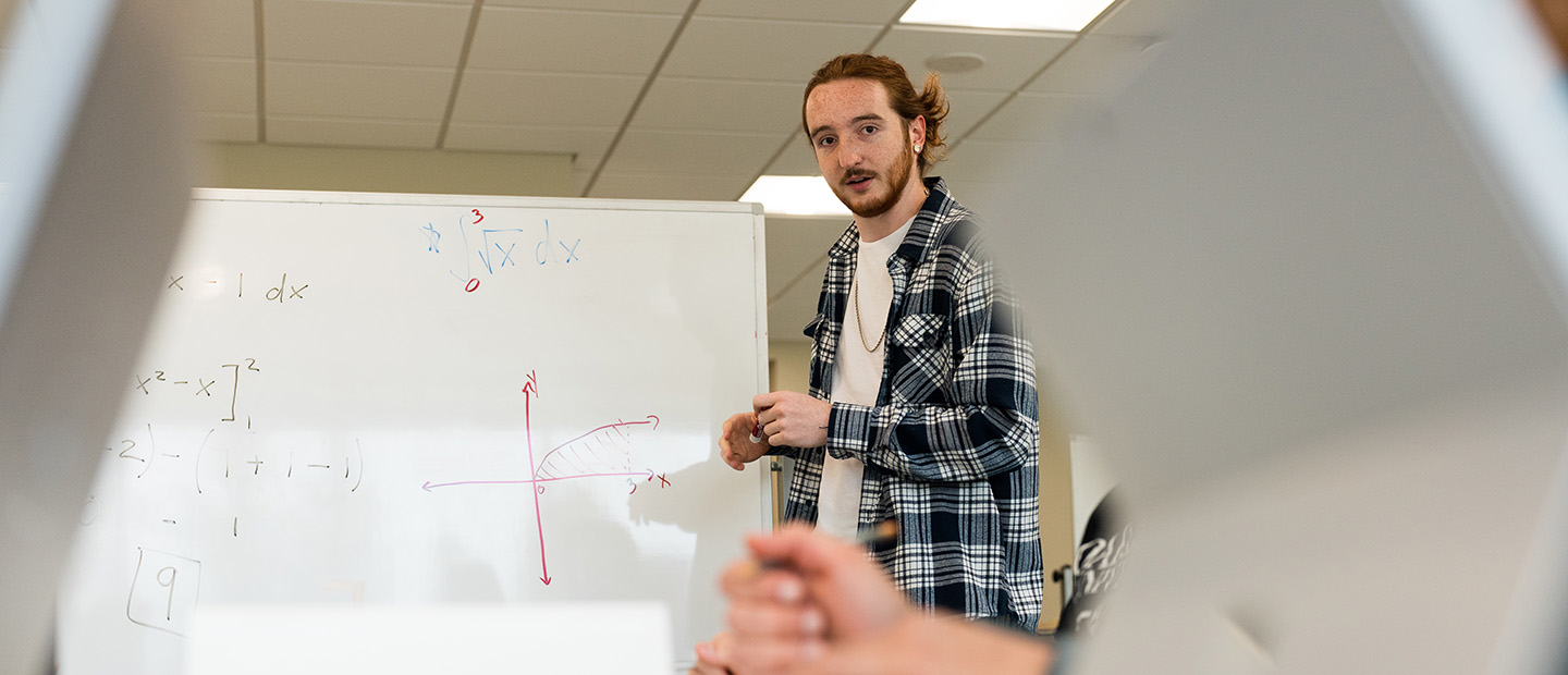 A man writing equations on a white board