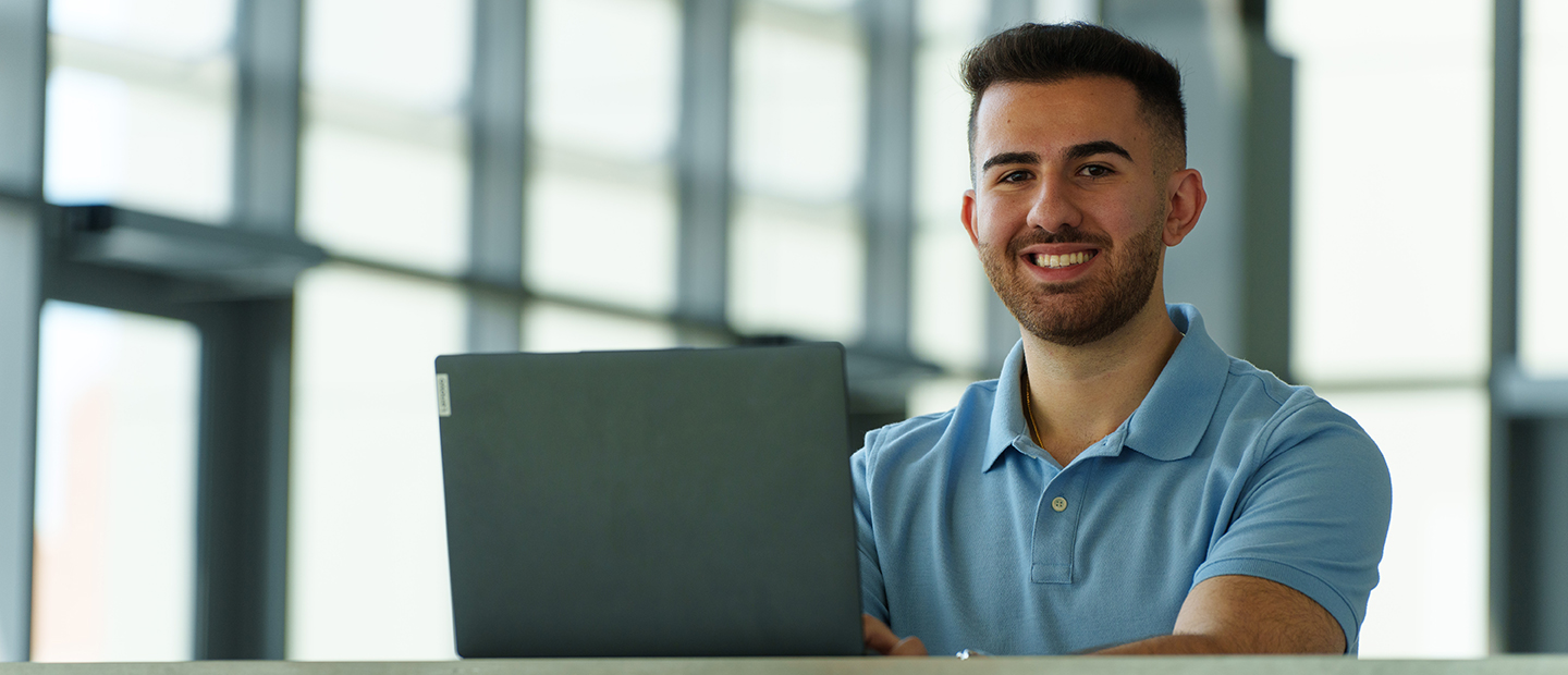 SECS Department Undergraduate Programs IT Banner A young man with a laptop smiling at the camera