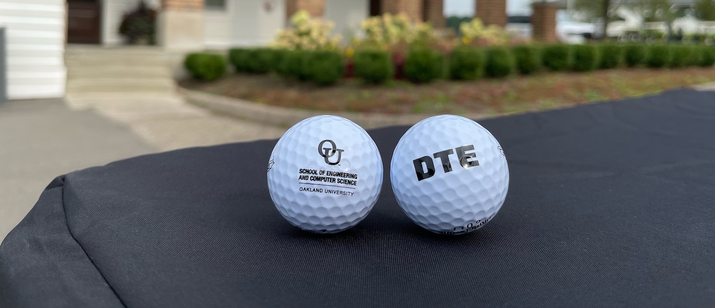 Golf Outing Two golf balls sitting on a table, one with a DTE logo and one with an OU logo