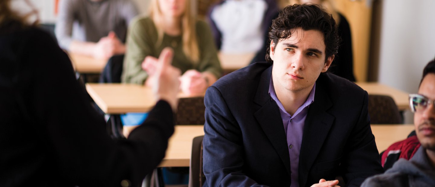 young man in classroom young man in a classroom full of students, watching someone at the front of the room