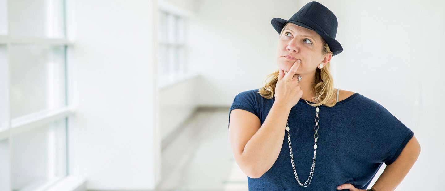 woman thinking woman in a blue shirt and hat with her hand on her chin and an inquisitive look on her face