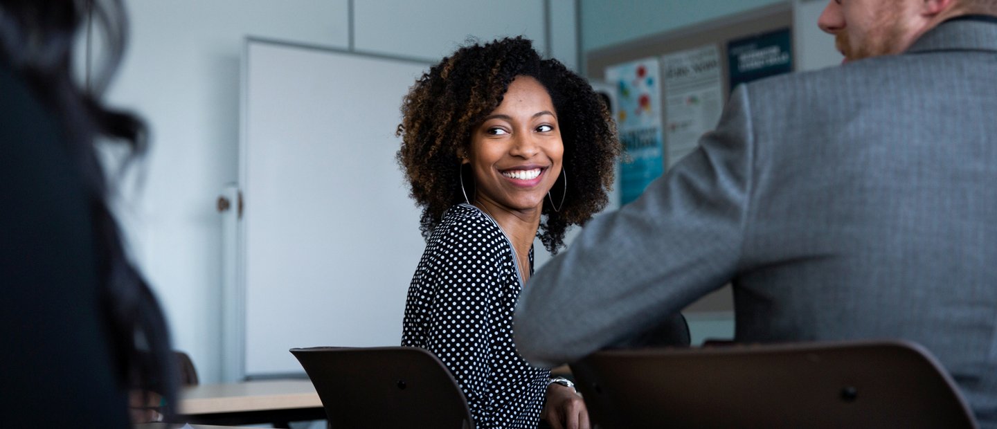 student smiling in class man and woman seated at desks, looking over their shoulders at someone behind them