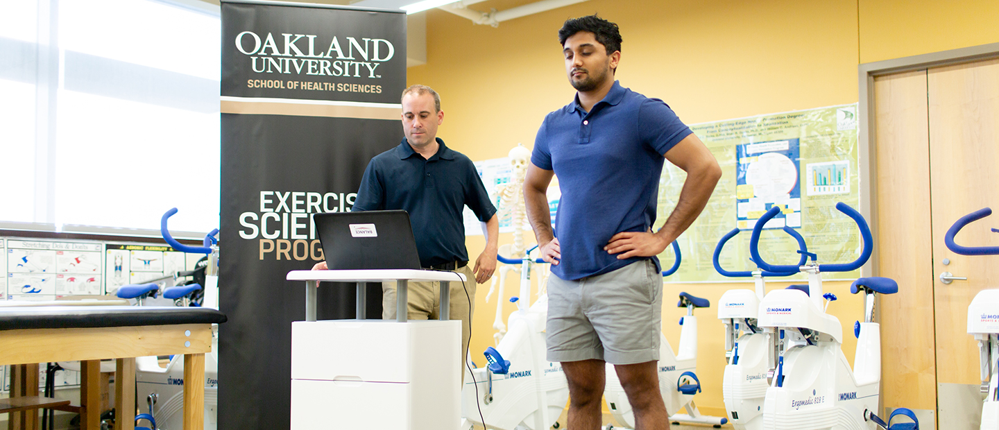 Exercise research A man standing on a scale while another man reads data on a computer screen, in a fitness studio.