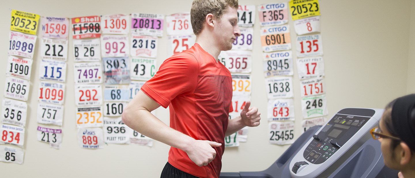 person running on treadmill image of a person running on a treadmill with a second person monitoring the treadmill statistics