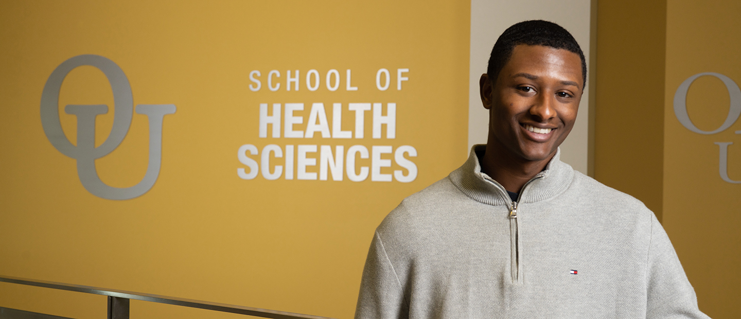 student standing in the Human Health Building image image of a student standing in the Human Health Building in front of a sign with the interlocking OU and School of Health Sciences text