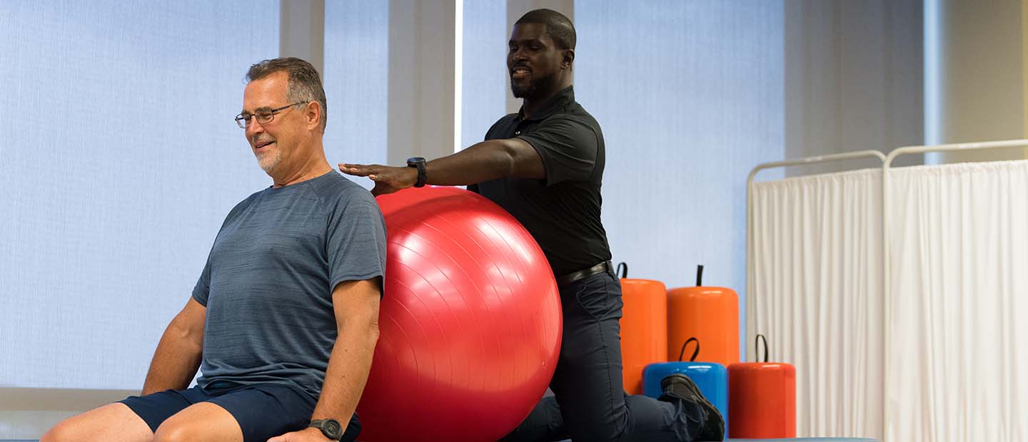 Physical therapy A male physical therapist helping a man with an exercise ball on a table in a fitness studio.
