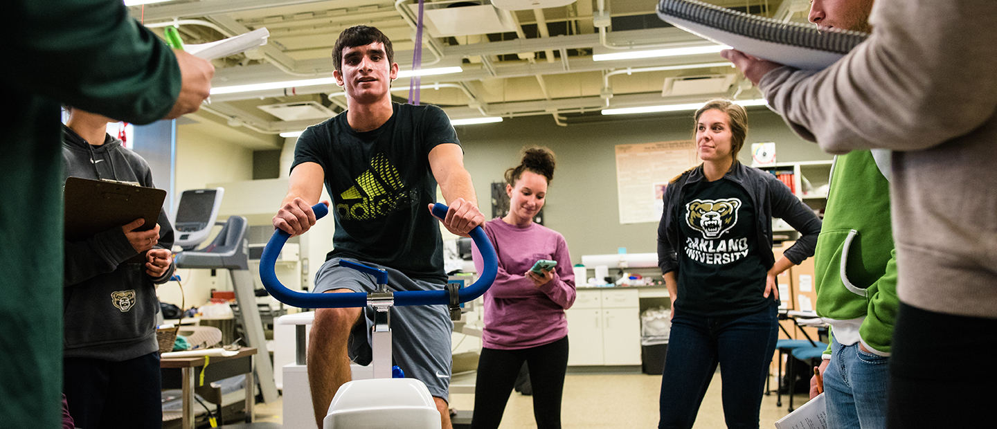 man exercising image of a man riding a stationary bike in a lab while people watch and take notes