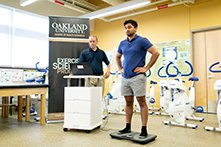 Man standing on an electronic device in an exercise science classroom with fitness equipment.