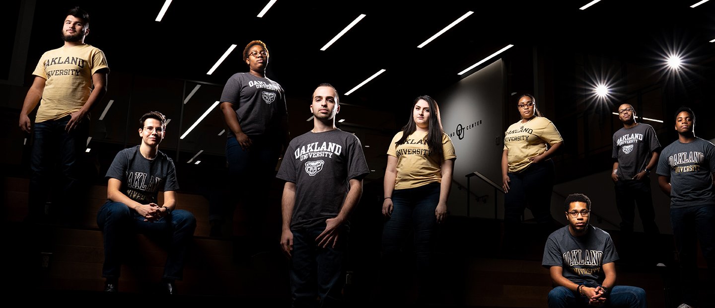 OU Climate Survey Banner An artistic photo of a group of students, some standing and some sitting, in a dark room with spotlights.