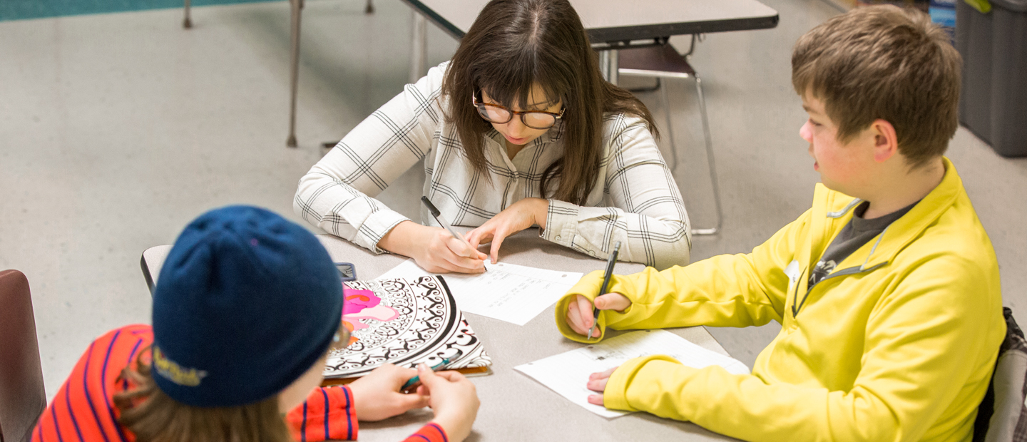 An aerial photo of three kids seated at a table, writing An aerial photo of three kids seated at a table, writing.