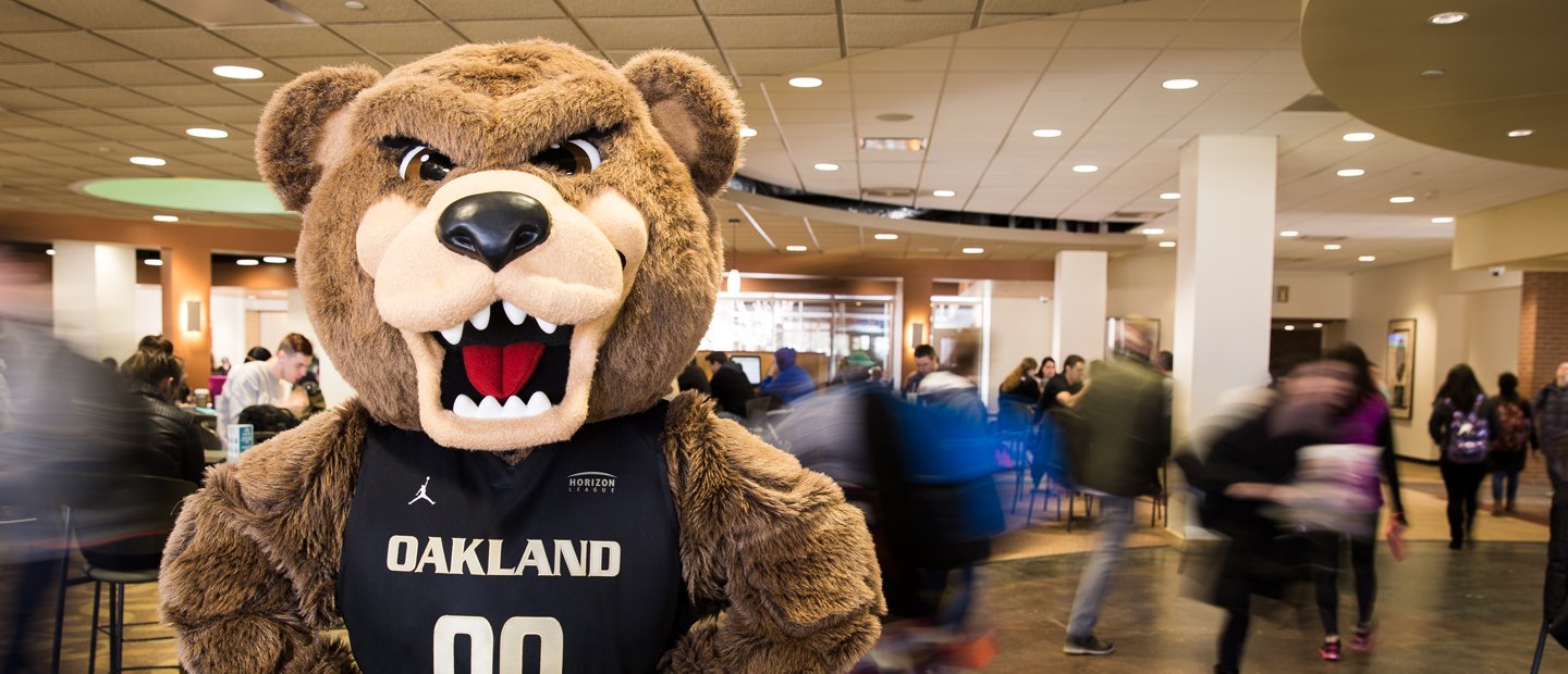 The Grizz bear The Grizz bear wearing a jersey that says Oakland on it, with people walking through the room behind him