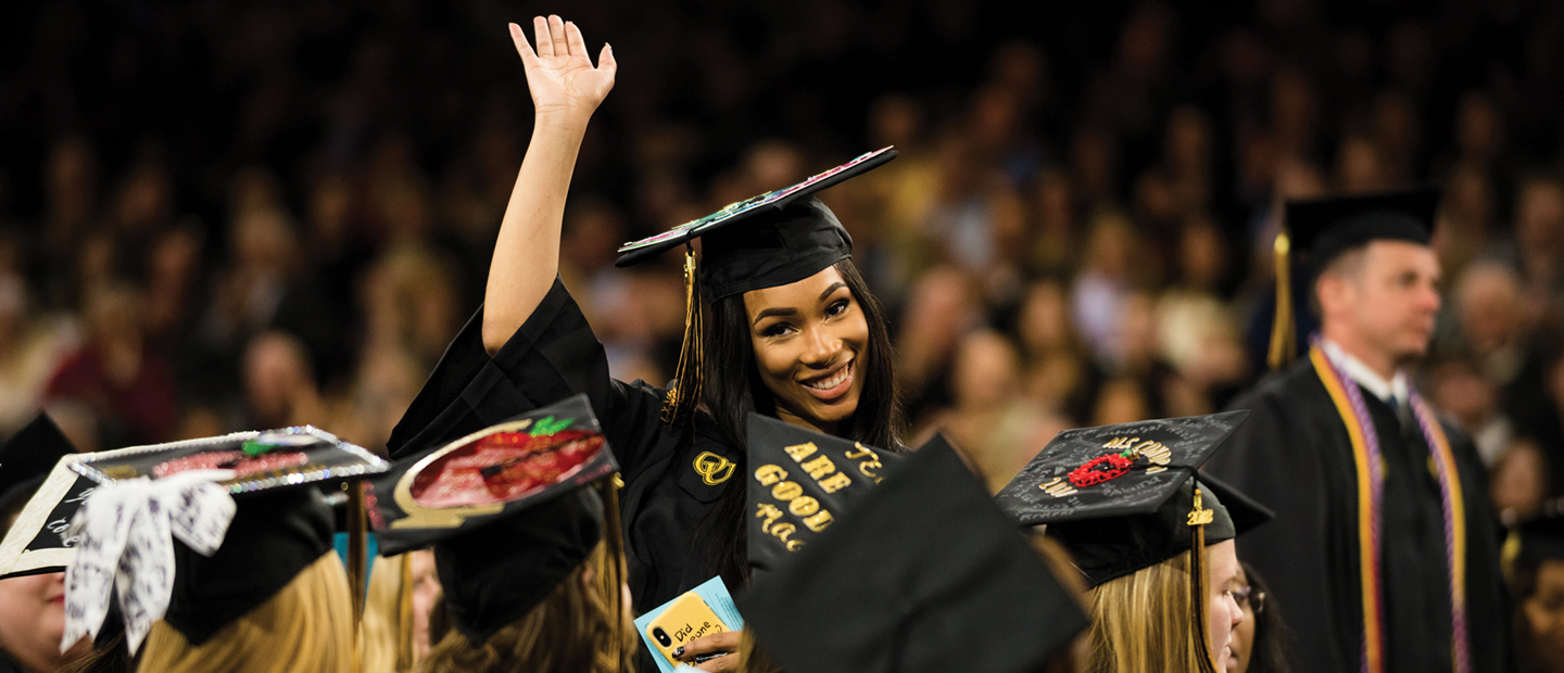 Dream Initiative Banner Banner with a woman in here graduation outfit smiling and waving surrounded by other graduates.